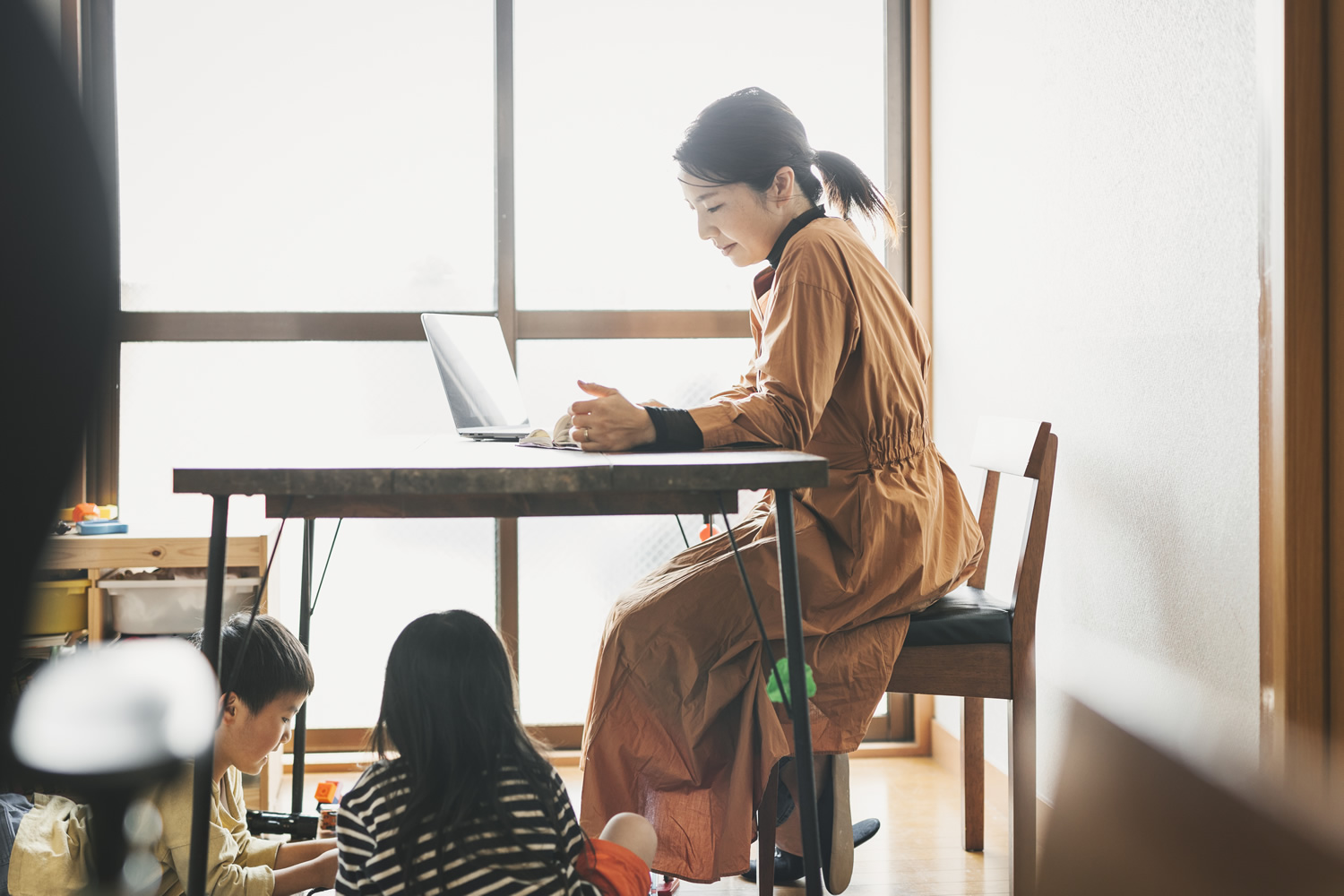 Asian mother working with laptop while her son and daughter are playing in the living room