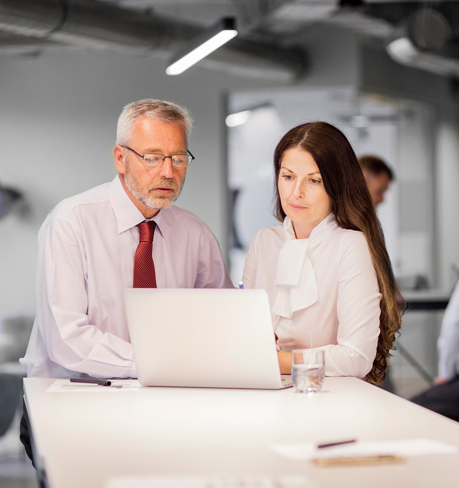 Senior businessman and businesswoman looking at laptop in the office